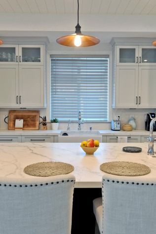 Kitchen island with marble countertop, cabinets, and a hanging light. Fruit bowl and placemats on the island.