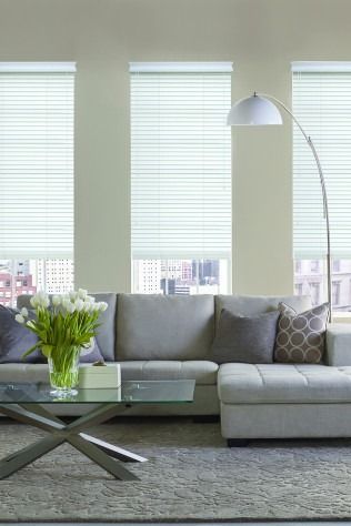 Living room with light gray sectional sofa, tall windows with blinds, arched floor lamp, glass coffee table, and city view.