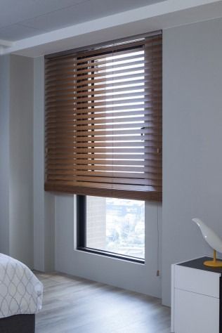 Window with partially open brown wooden blinds in a room with a bed and a nightstand.