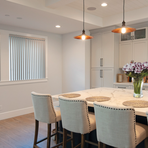 Modern kitchen with island, bar stools, pendant lights, and window with blinds.
