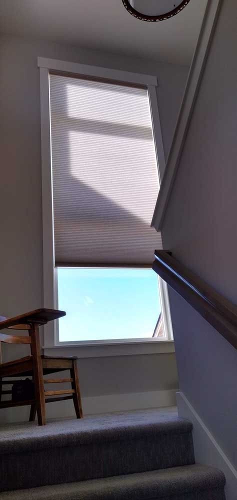 Window with drawn shade above a staircase; blue sky visible through the window.