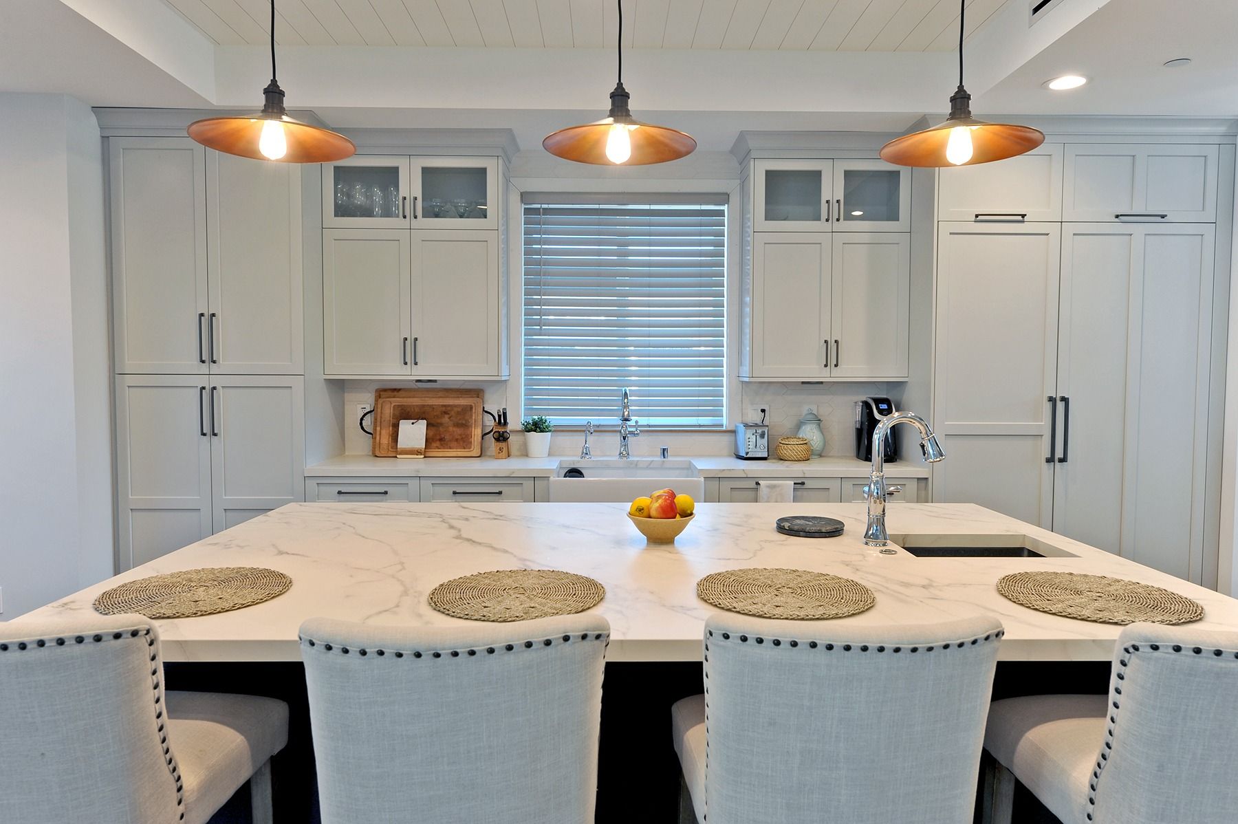 Kitchen with white cabinets, large island with seating, pendant lights, and window.
