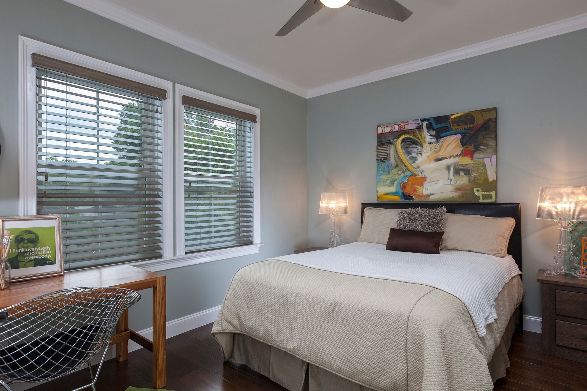 Bedroom with bed, desk, artwork, windows with blinds, and blue-green walls.