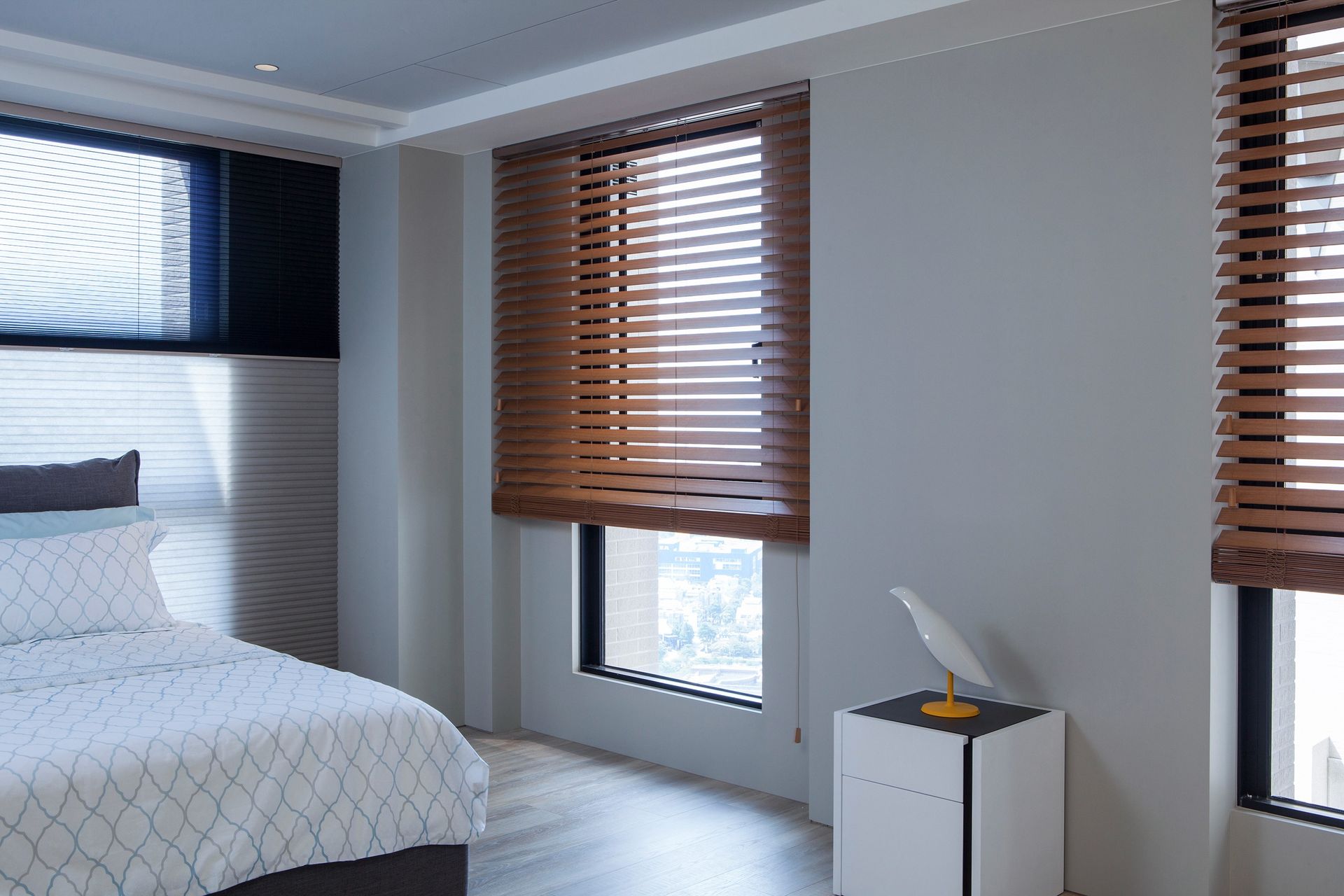 Bedroom with a bed, two windows with wooden blinds, and a small side table.