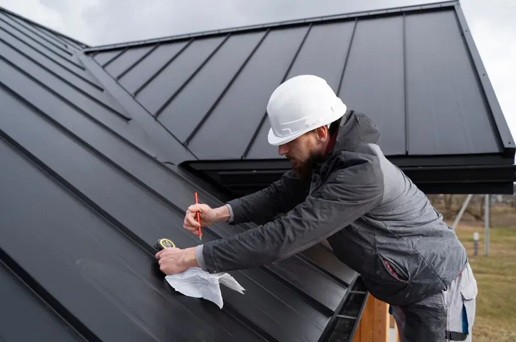 A man wearing a hard hat is working on a roof.