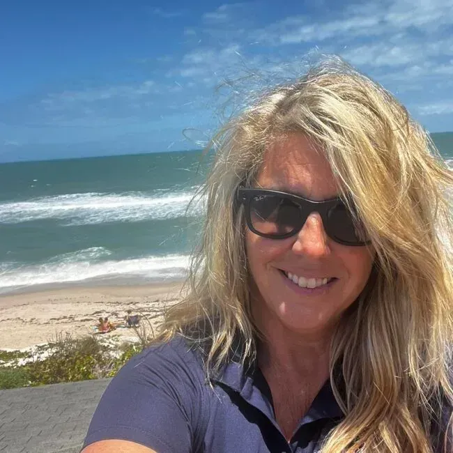 A woman wearing sunglasses is smiling in front of the ocean