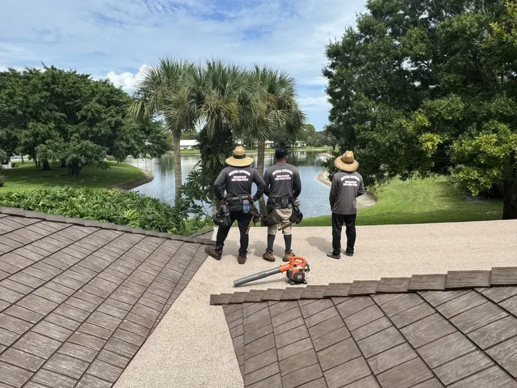 Three men are standing on top of a roof next to a lake.