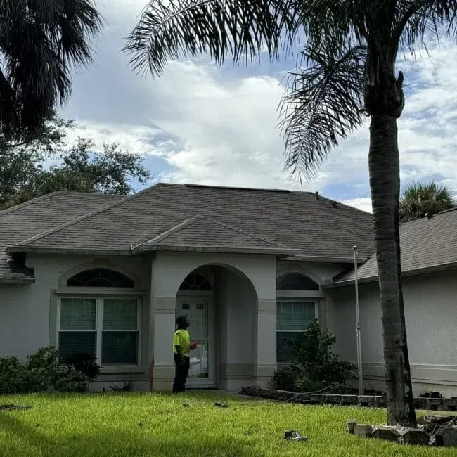 A man is standing in front of a house with a palm tree in the foreground.