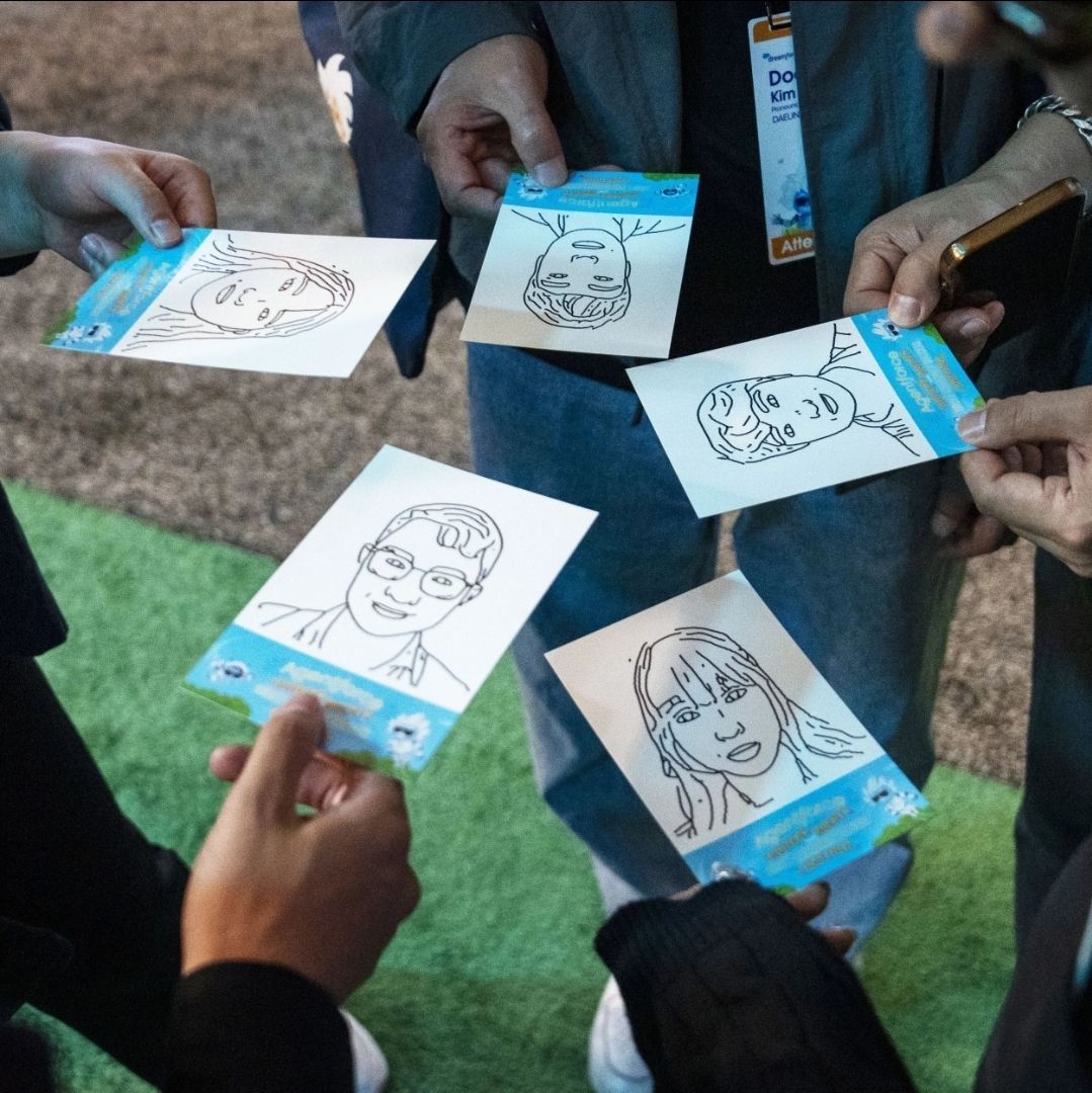 People holding up drawings of faces on blue cards. Green and gray background.