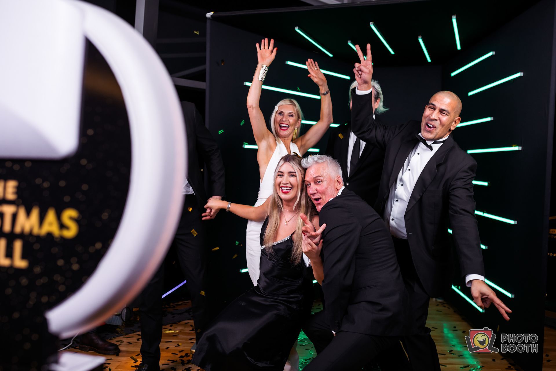 People pose for photo booth at a Christmas Ball, confetti falling. Black and white formal attire.
