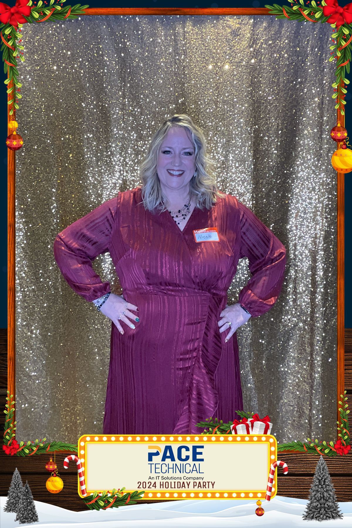 Woman in burgundy dress poses hands-on-hips at a holiday party photo booth, glitter background, festive frame.