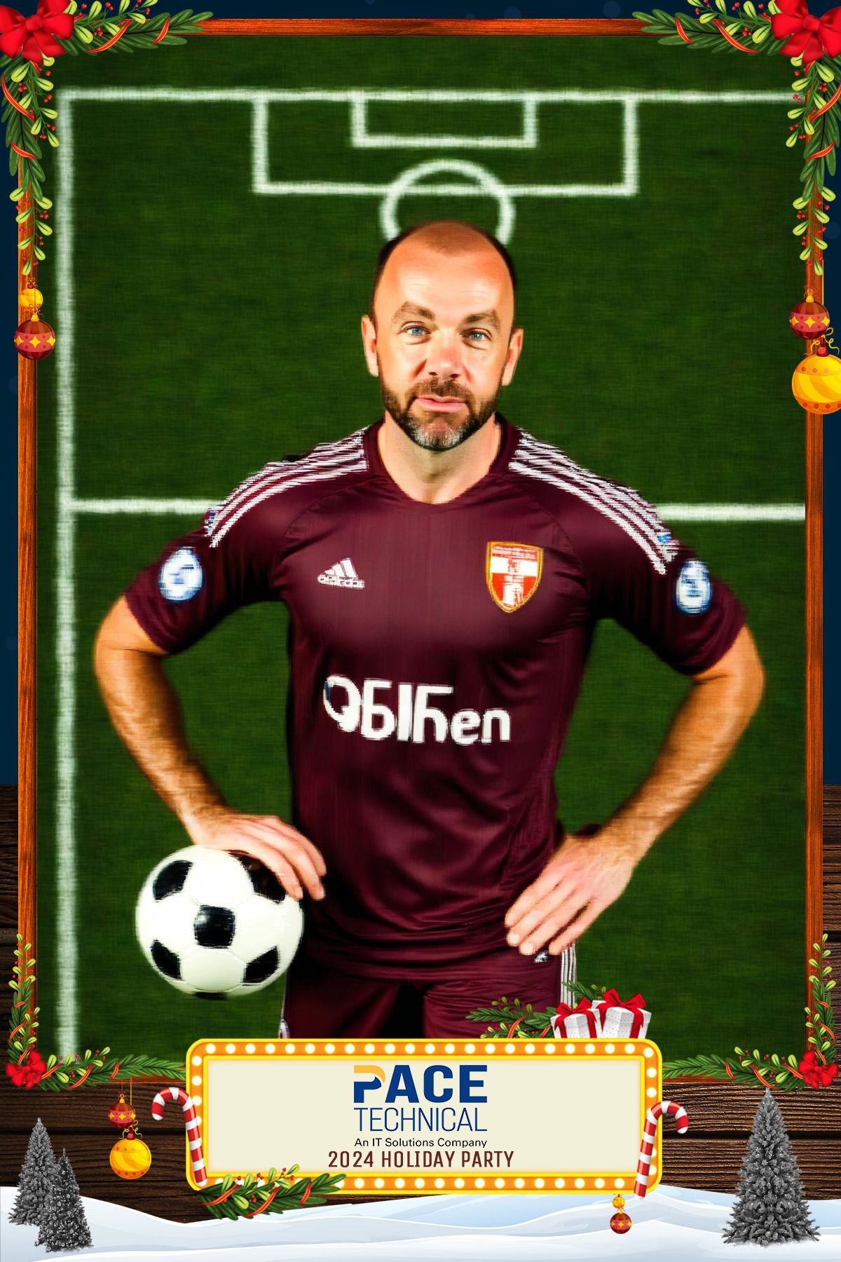 Man in maroon soccer uniform holding a soccer ball, in front of a soccer field background.