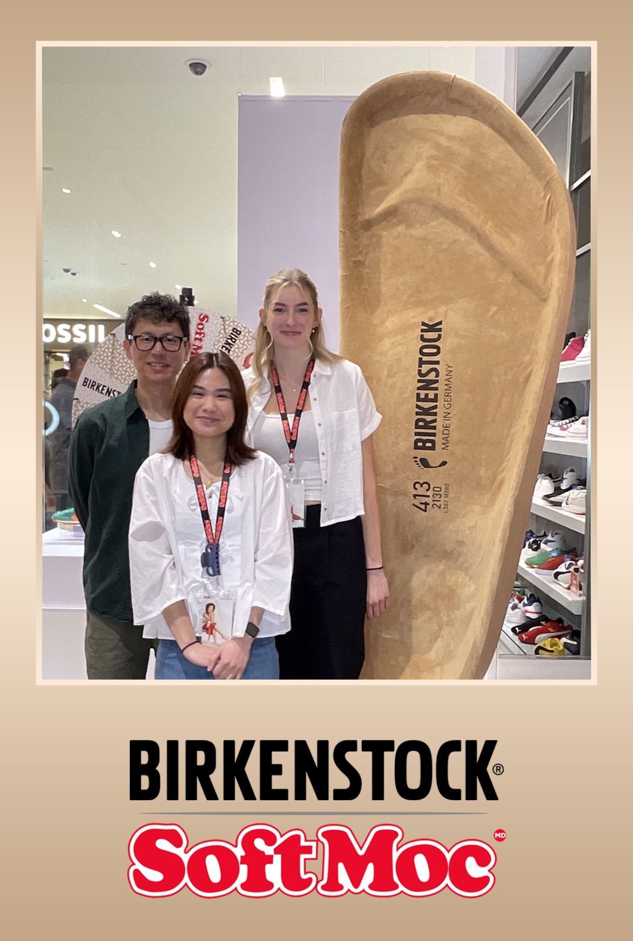 Three people pose with a giant Birkenstock sandal in a store. The Soft Moc logo is below.