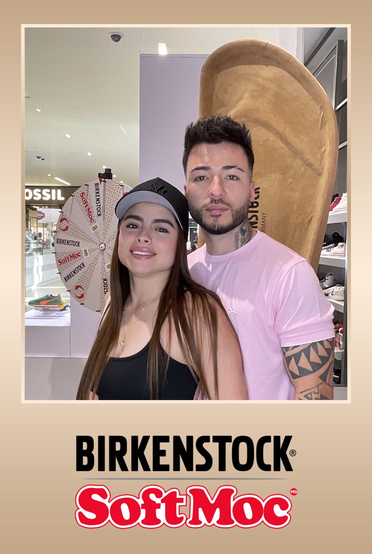 Couple at Birkenstock/SoftMoc store, woman in black top, man in pink shirt, near a prize wheel.