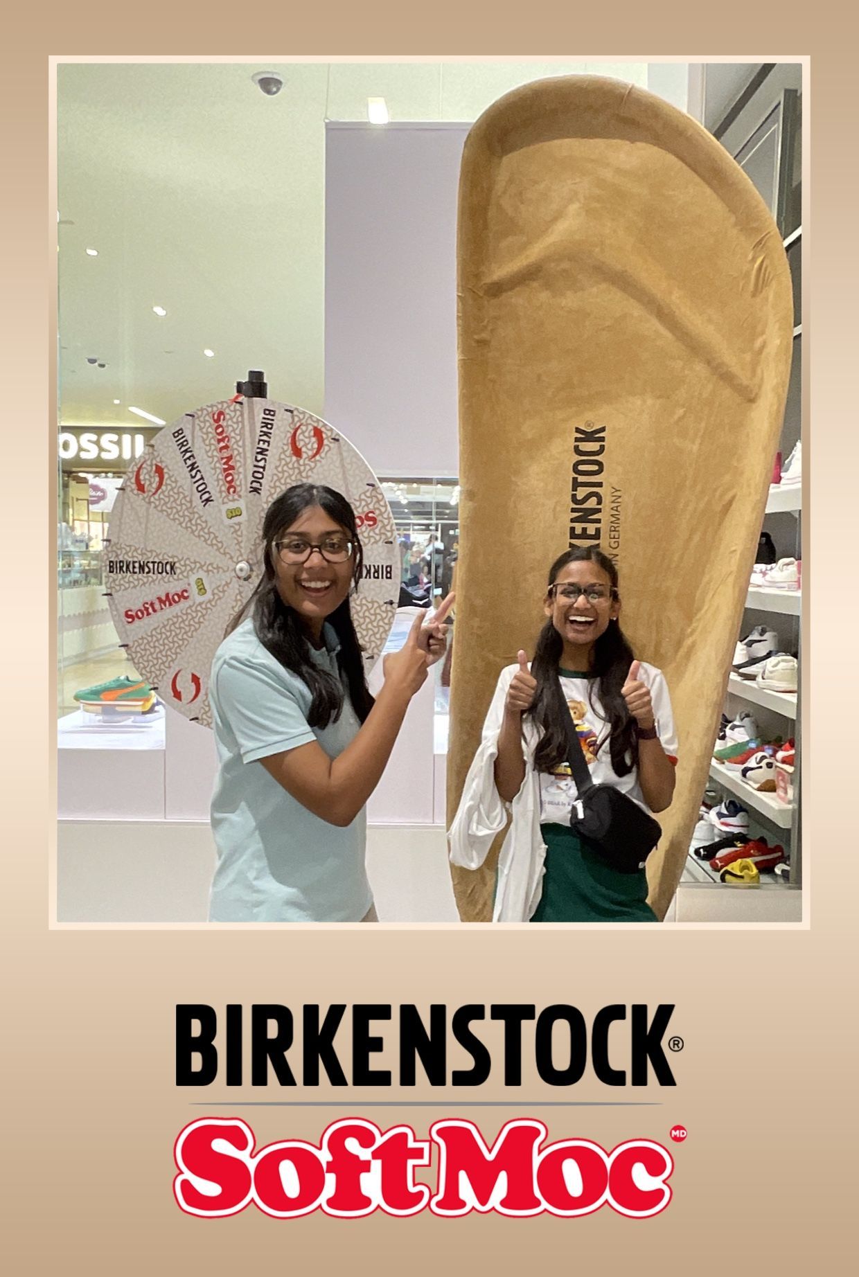 Two people at a Birkenstock display; one spins a prize wheel, the other poses with a giant shoe, thumbs up.