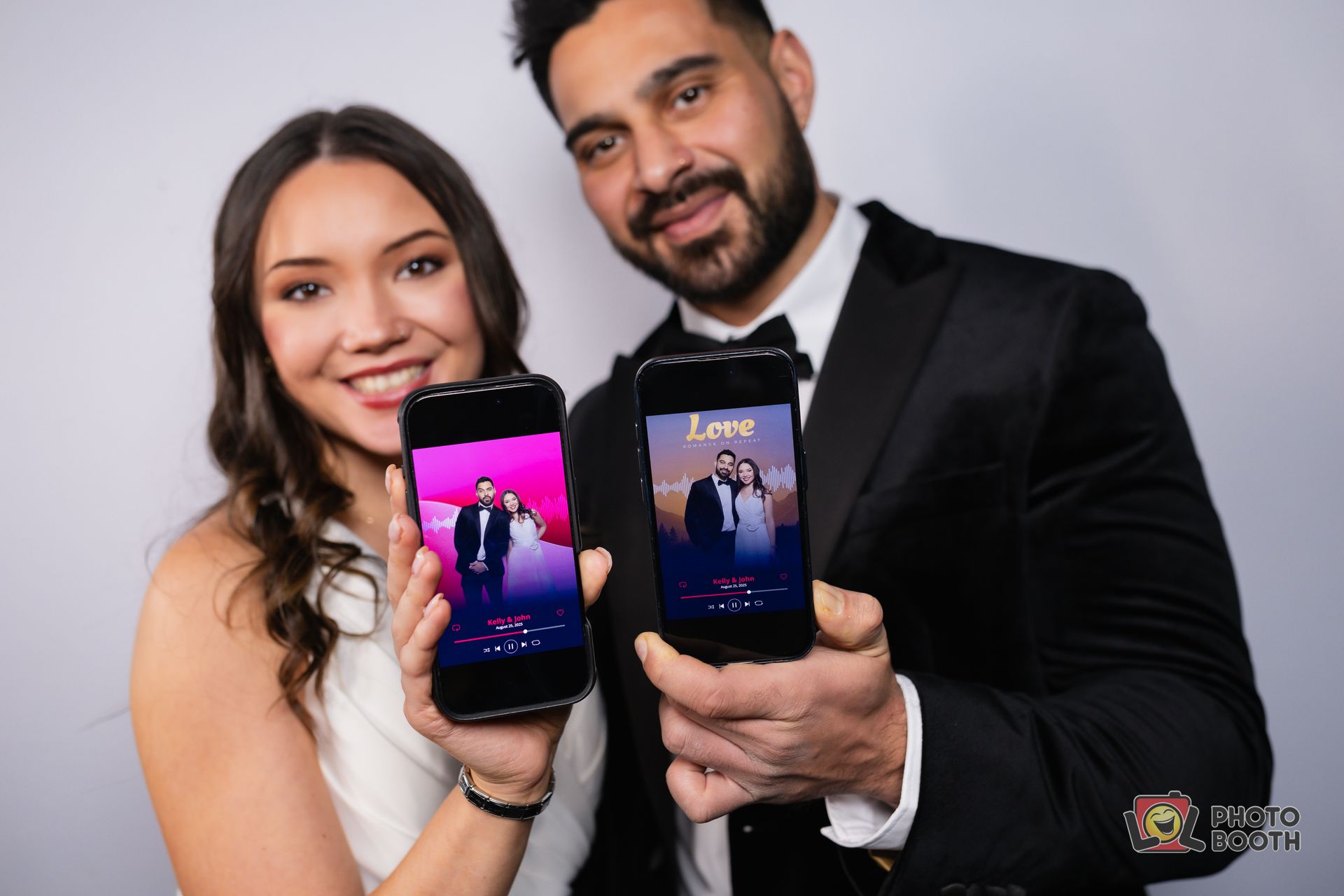 Couple holding phones with wedding photos; both smile, white backdrop.