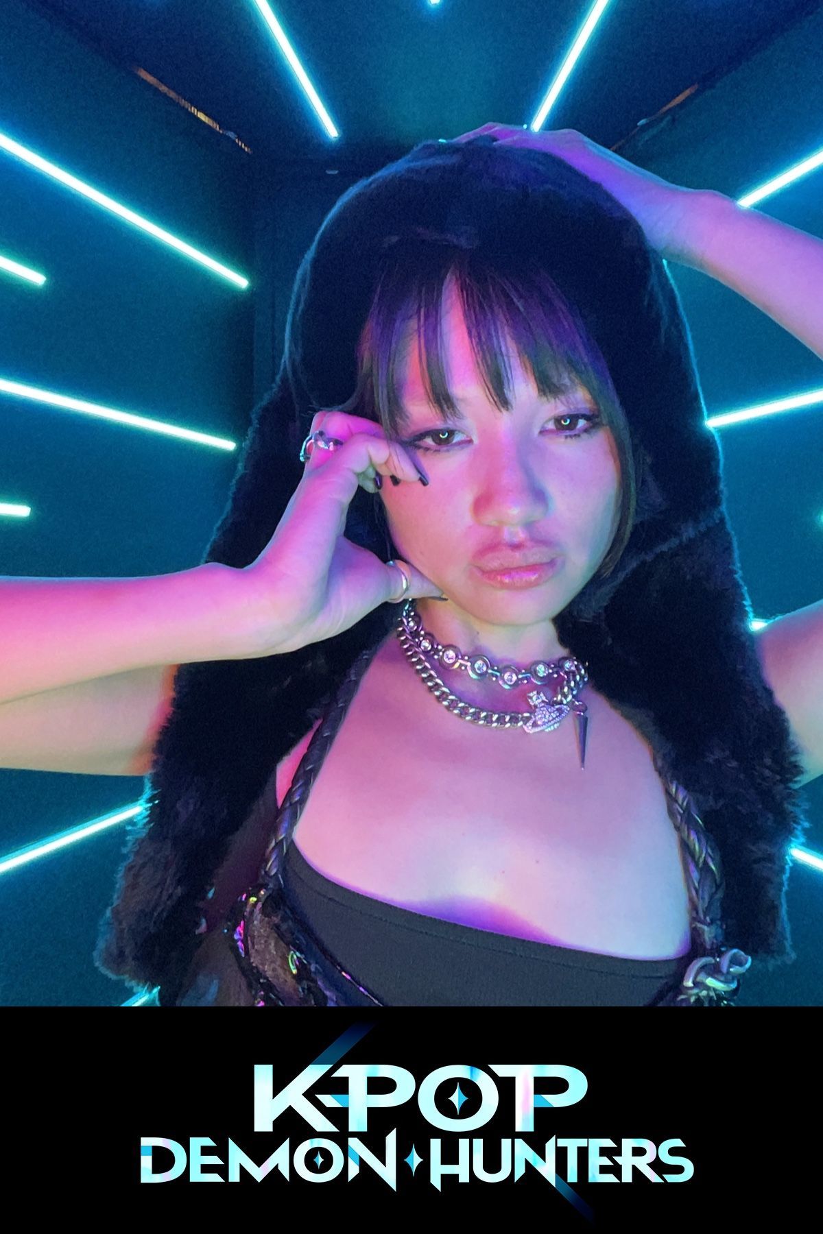 Woman in dark outfit poses with hands on head, surrounded by neon blue lights.