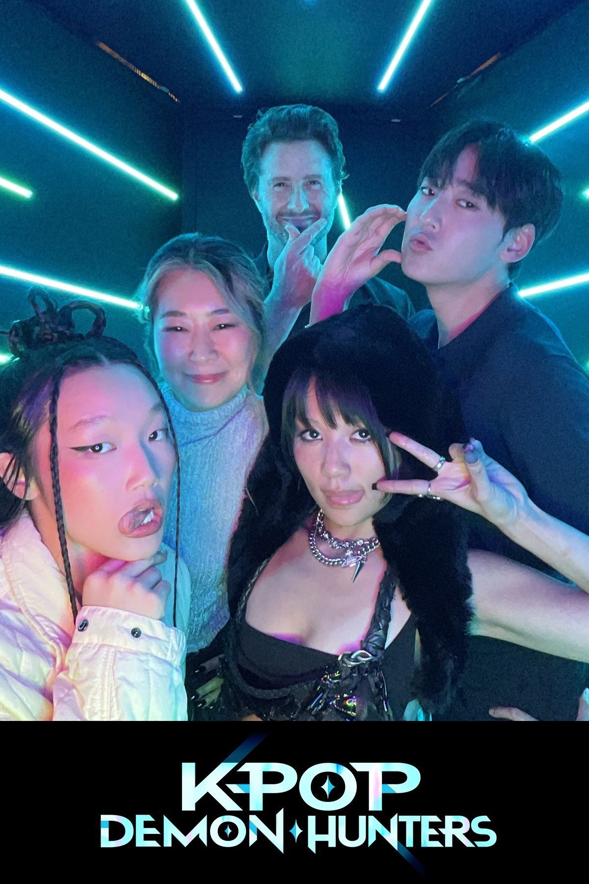 Group poses for photo with neon lights. “KPOP DEMON HUNTERS” logo at bottom.