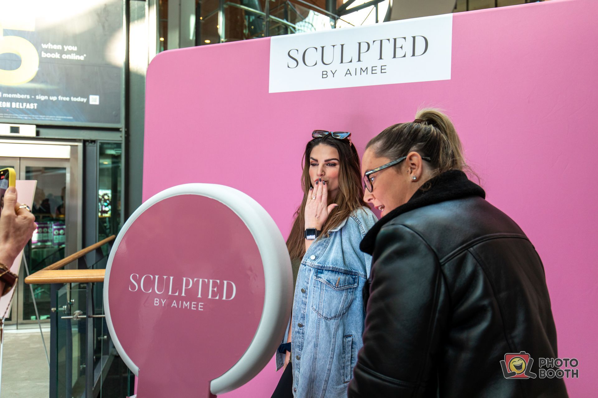 Two women pose at a pink photo booth with