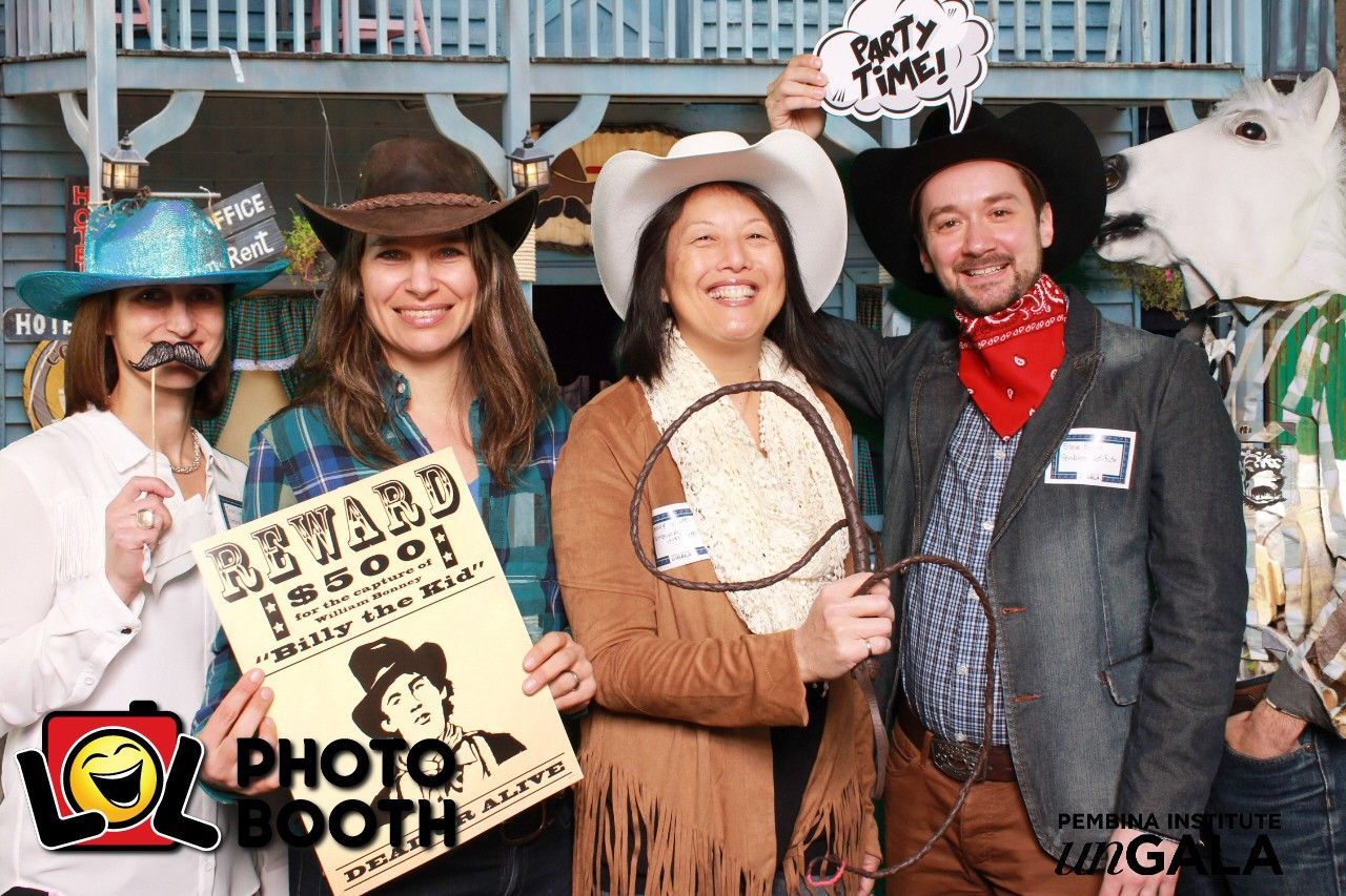 People in Western costumes at a photo booth; holding props, smiling.
