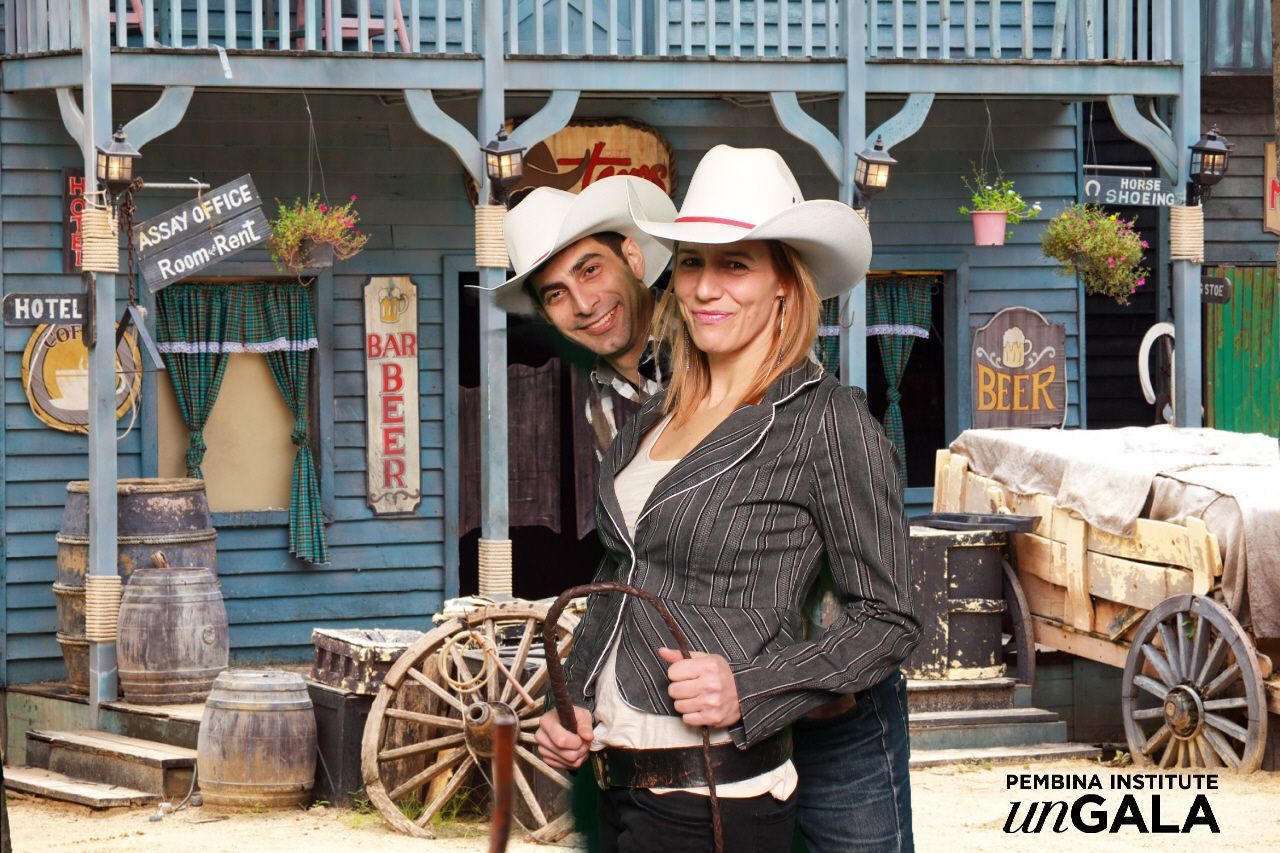 Couple in cowboy hats pose in front of a western-themed backdrop.
