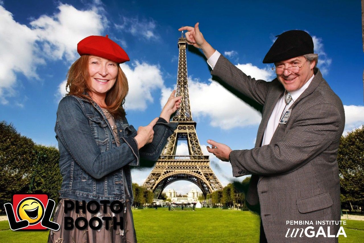 Two people in berets pose by Eiffel Tower. Woman points, man holds up object, both smiling.