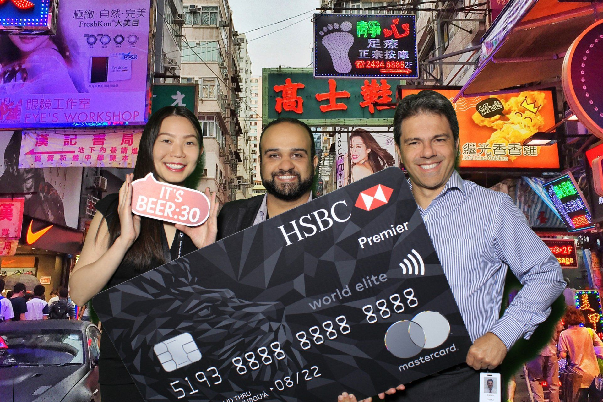 Three people holding a giant HSBC credit card in a Hong Kong street setting with neon signs.