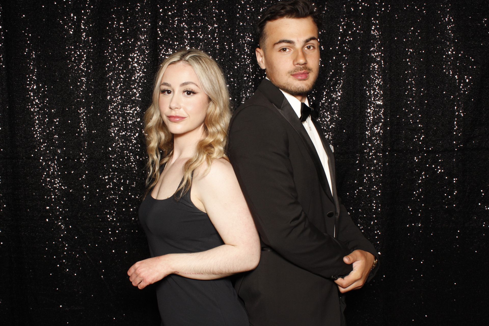 Couple posing back to back at a formal event, black sequined backdrop.