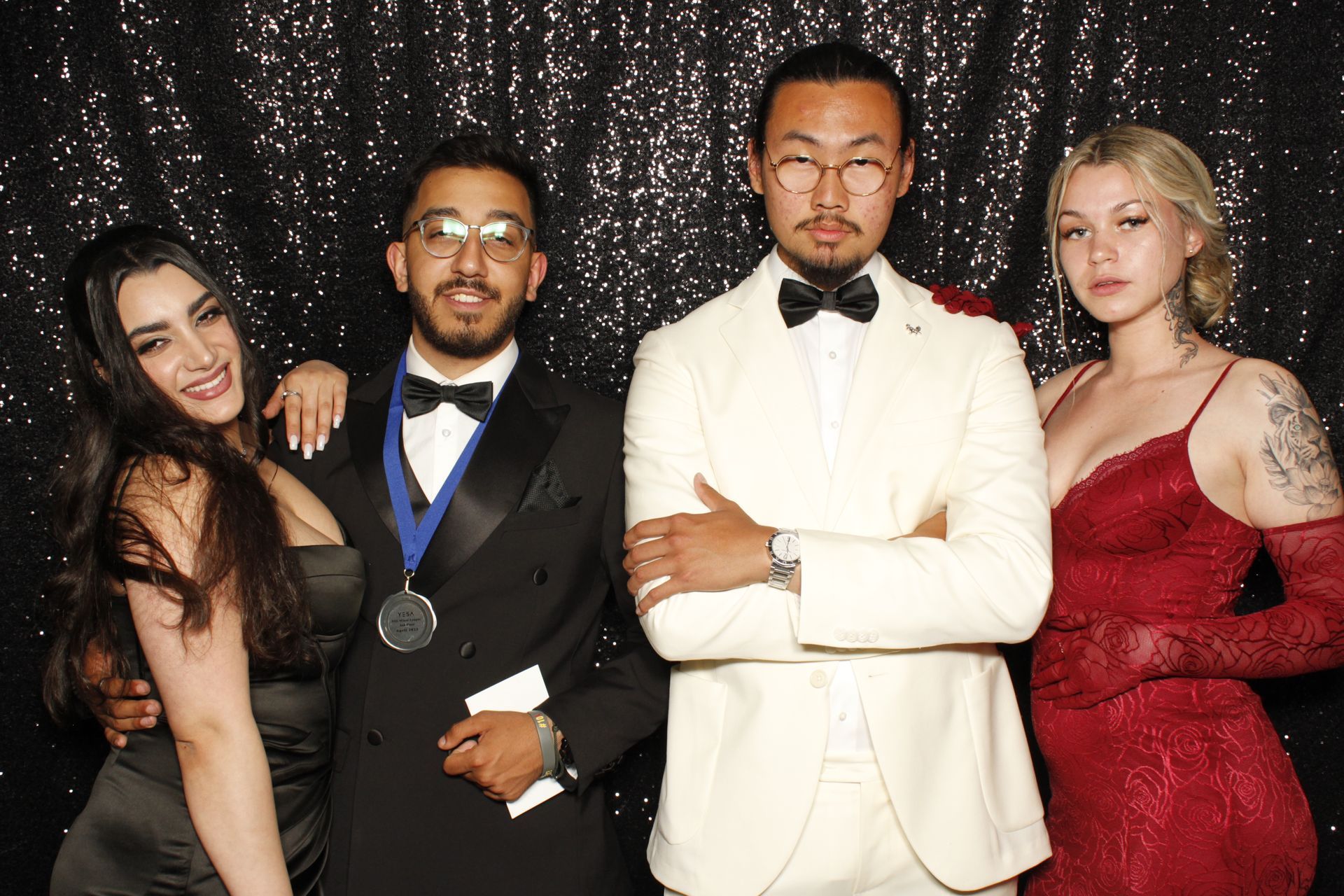 Four formally dressed people pose in front of a sparkly black backdrop.