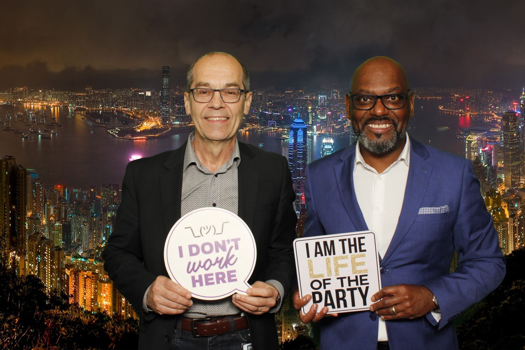 Two men holding party signs, posing in front of a city skyline backdrop.