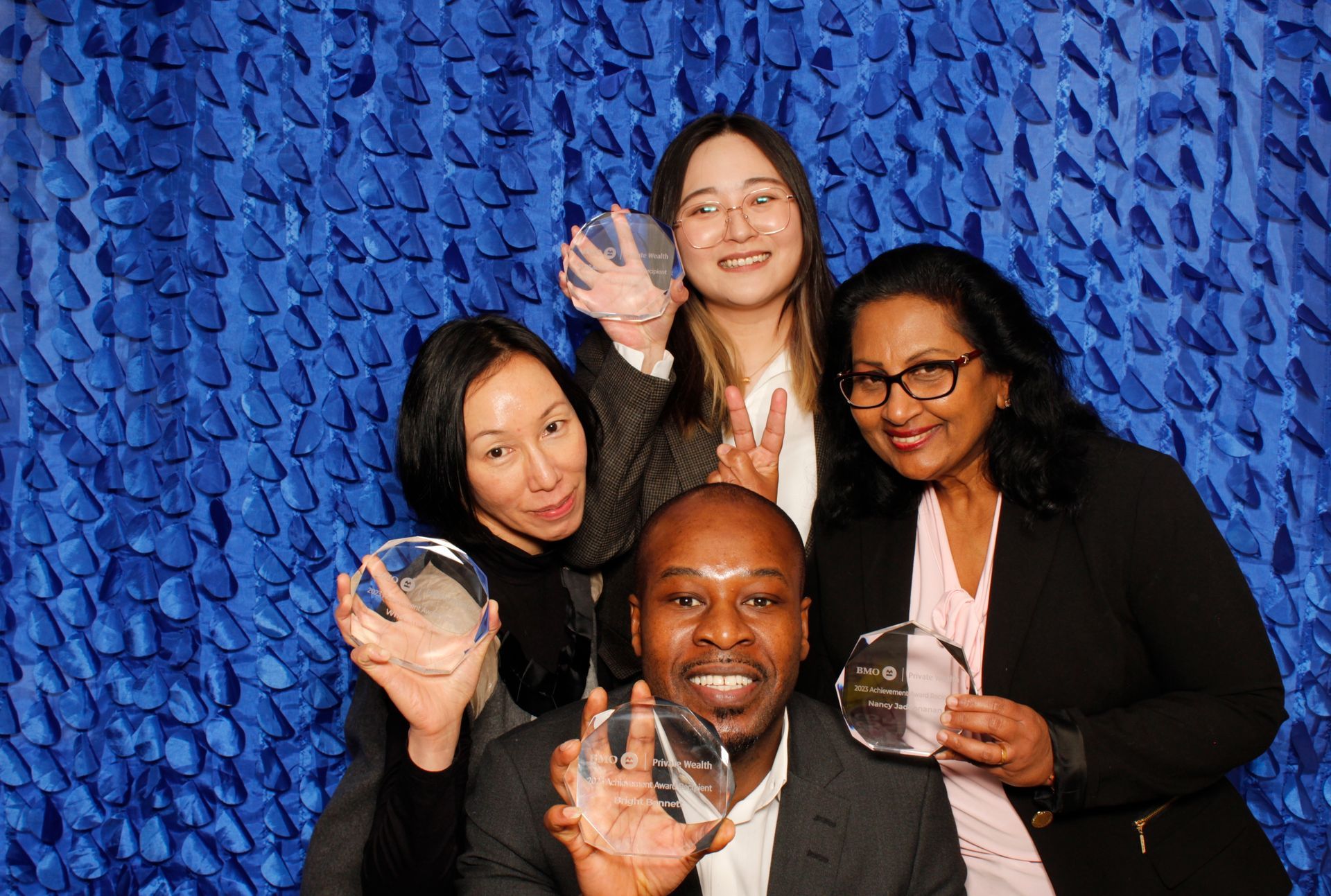 Group of people holding awards, smiling in front of a blue textured backdrop.