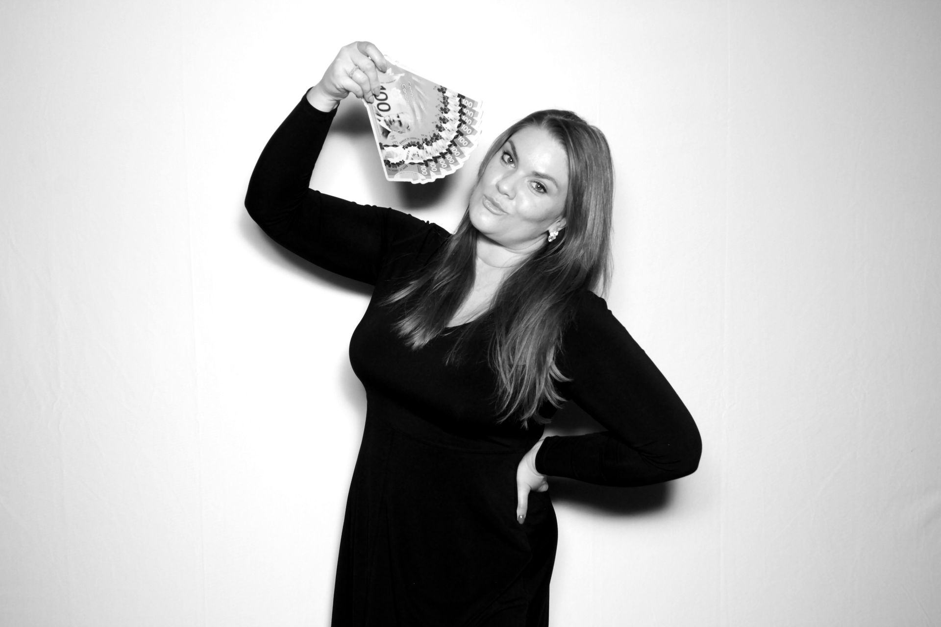 Woman in black dress holds up wad of cash, smiling. White backdrop.