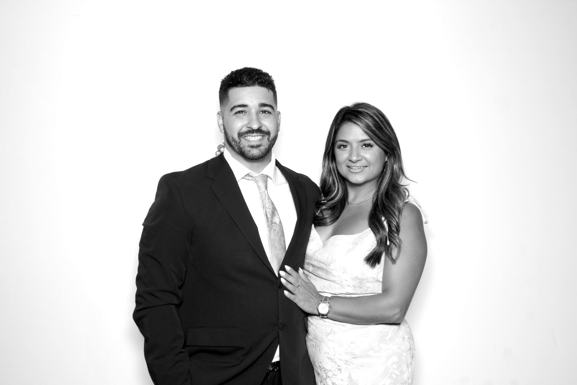 Formal portrait of a smiling couple posing in front of a white backdrop. Man in suit, woman in a dress.