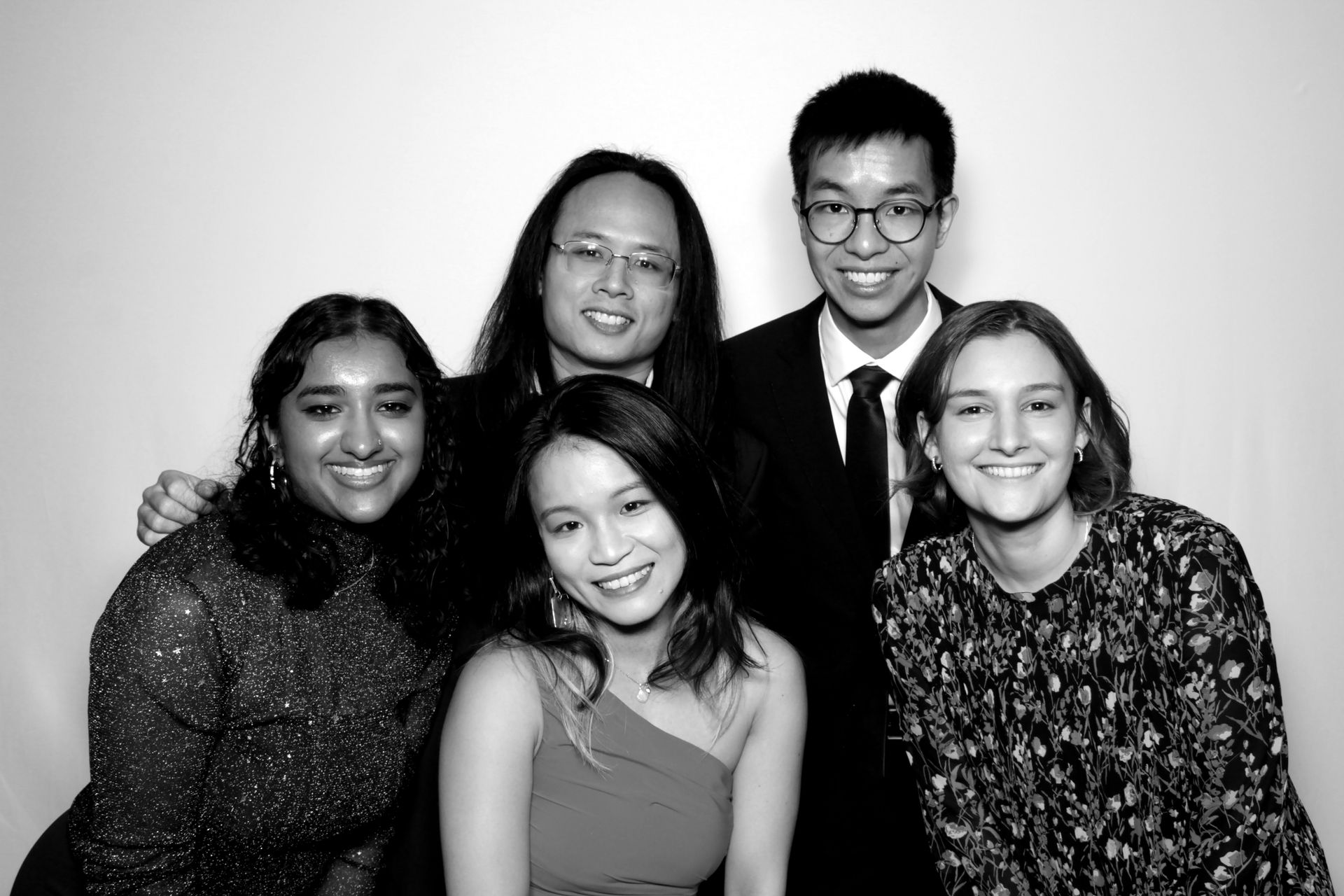 Five young people pose together for a photo, smiling against a white backdrop.