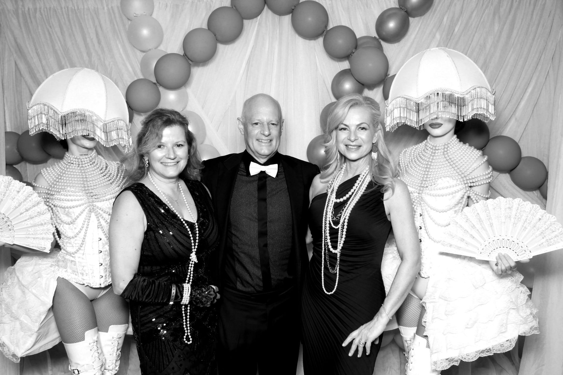Three people pose with costumed performers at a party, with balloons in the background.