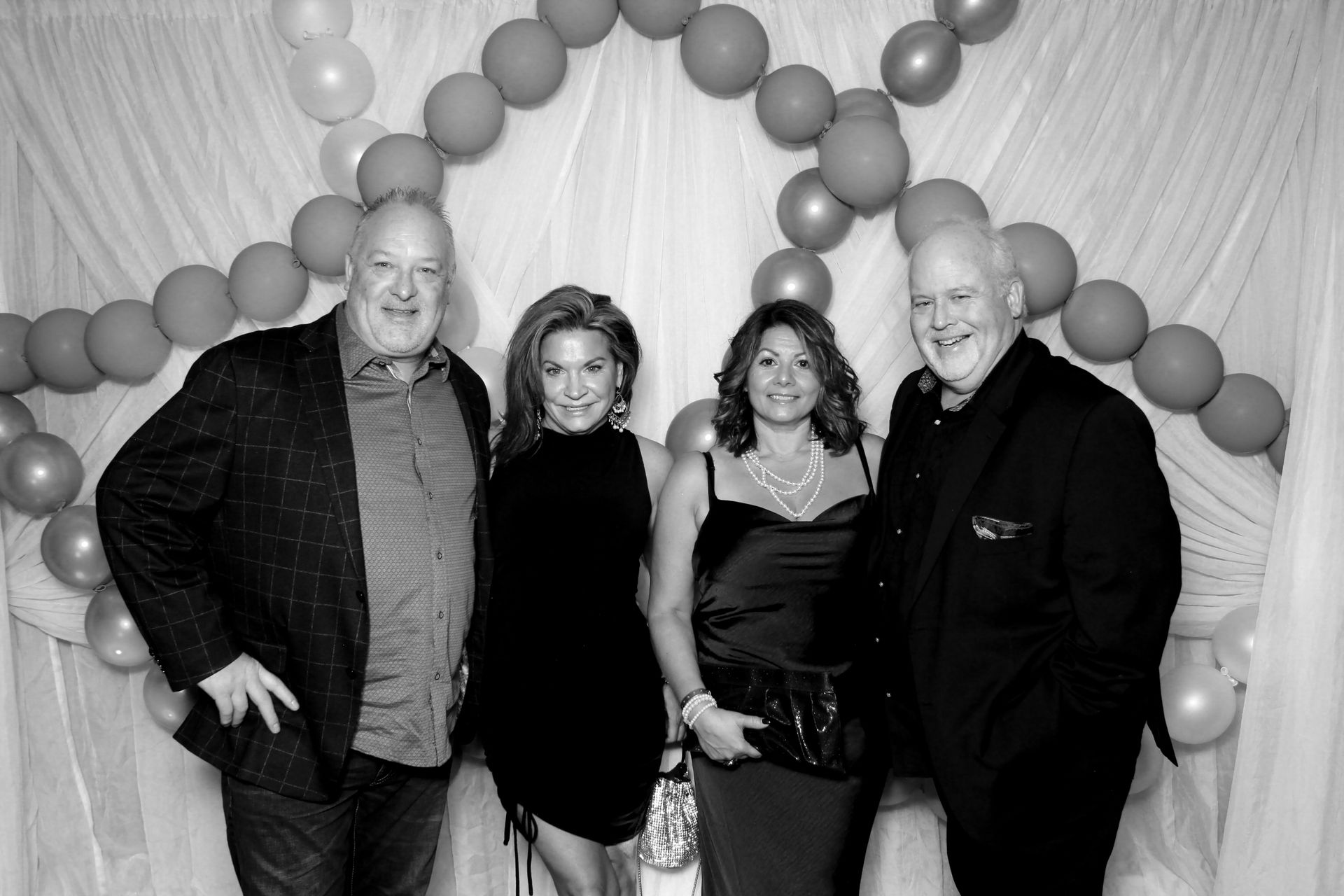 Four people posing for a photo. Balloons and fabric background.