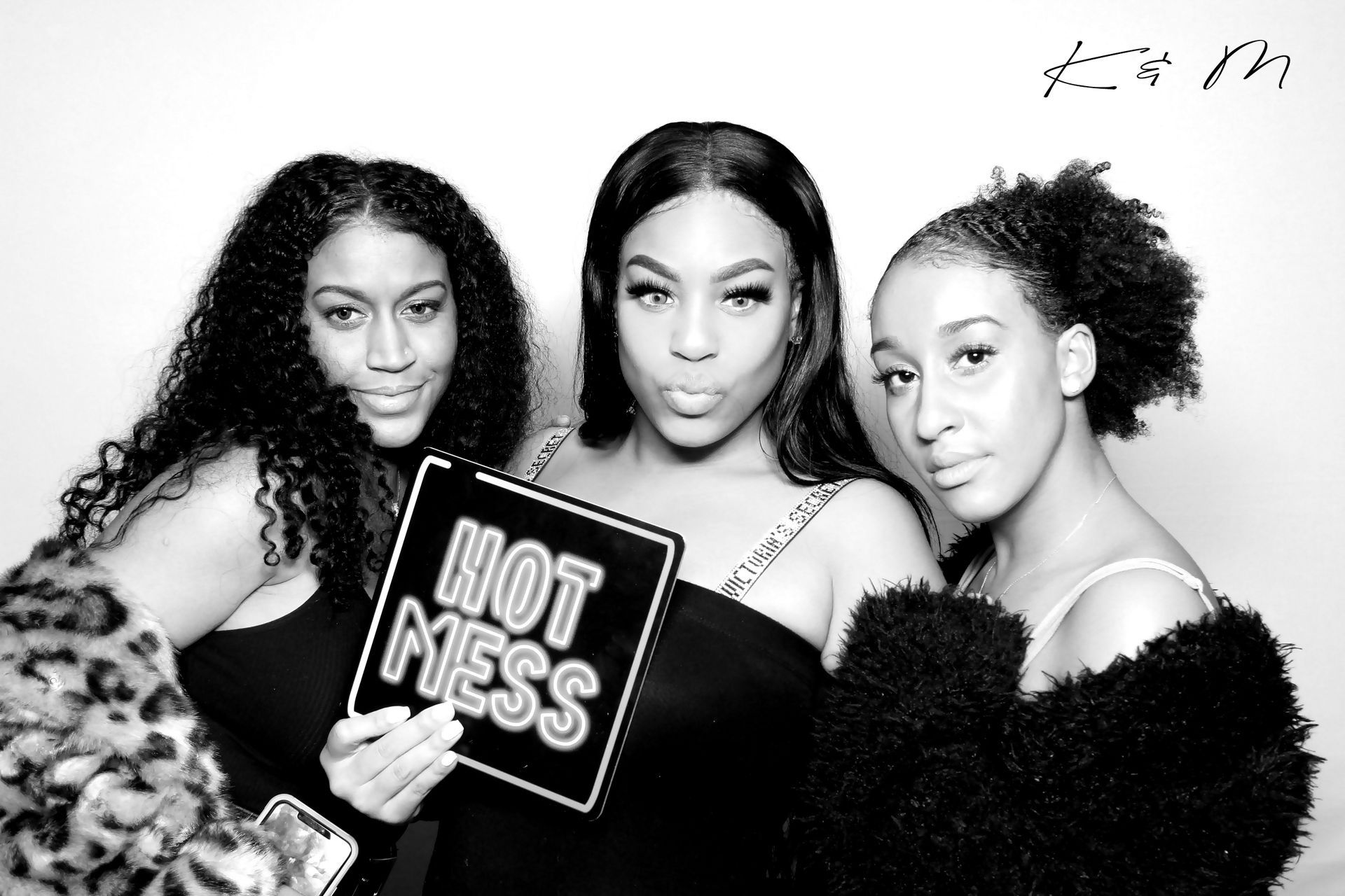 Three women posing for a photo booth. One holds a 