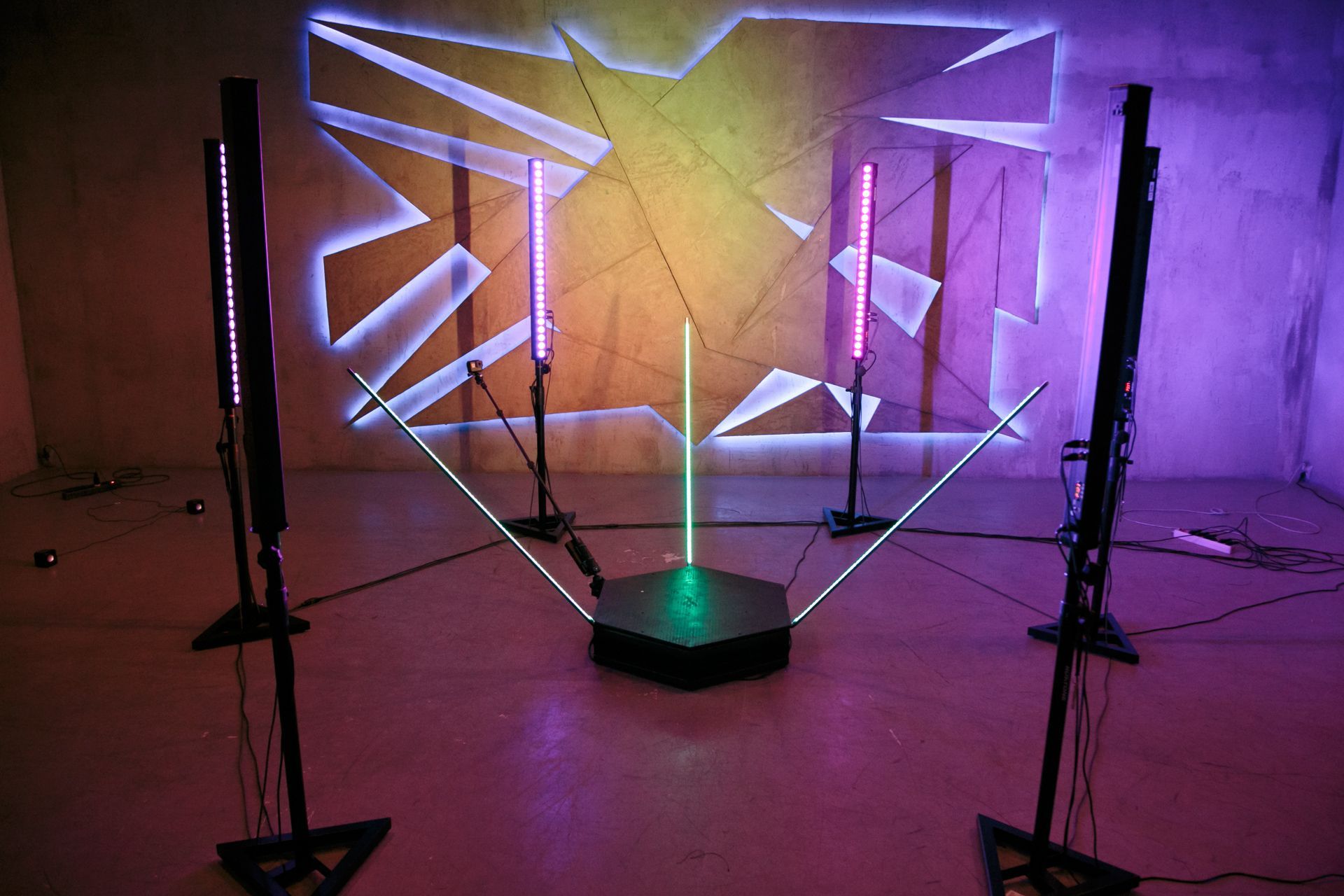 Installation art: Glowing geometric shapes and light bars in a room, illuminated with purple and green hues.