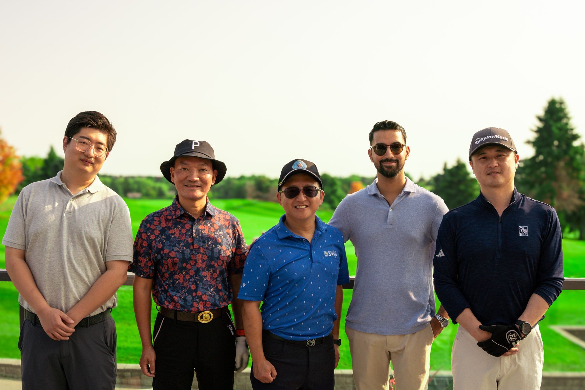 Five people smiling, posing outdoors on a golf course.