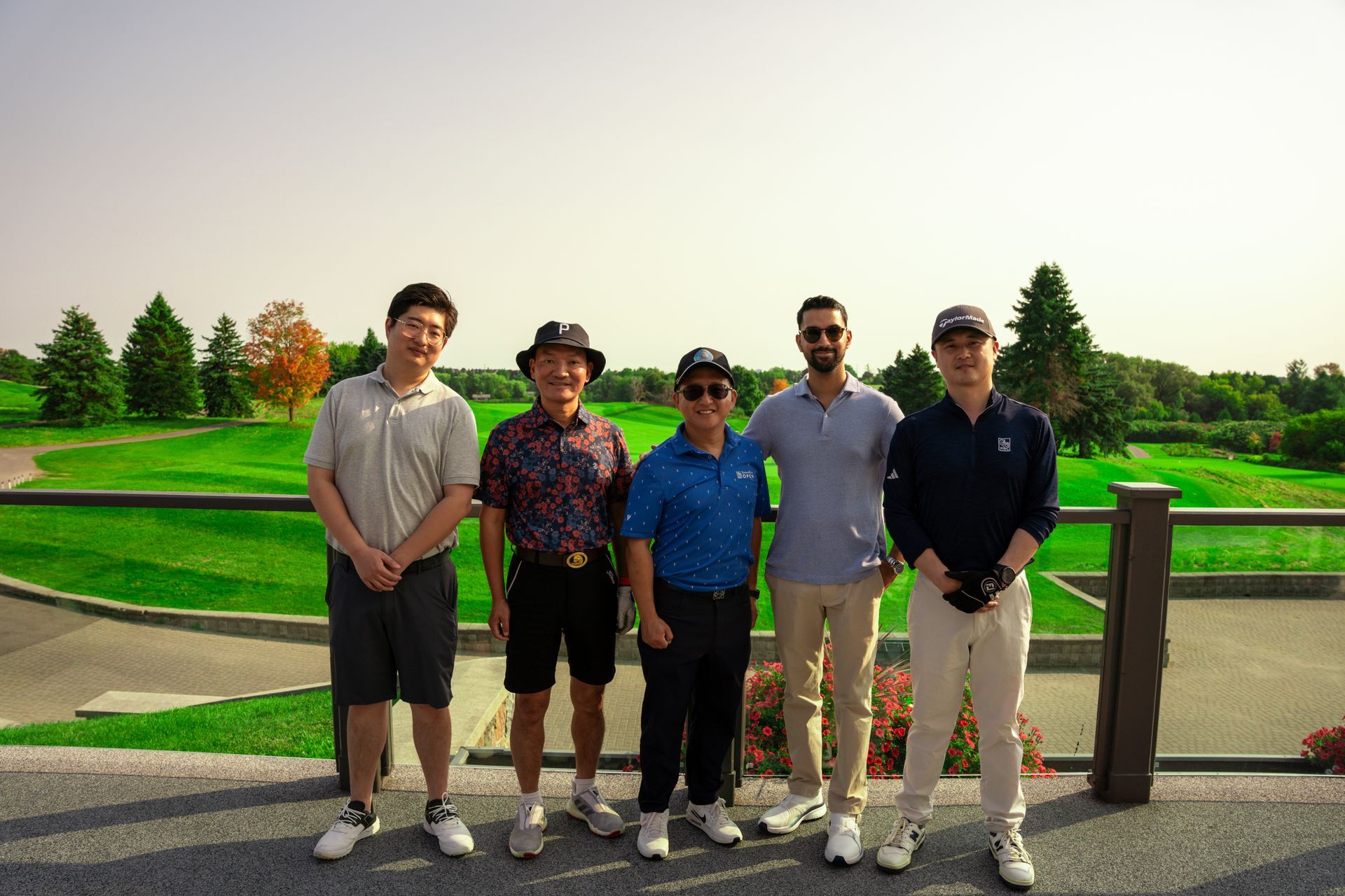 Five people standing on a paved area overlooking a golf course, smiling; sunny day.