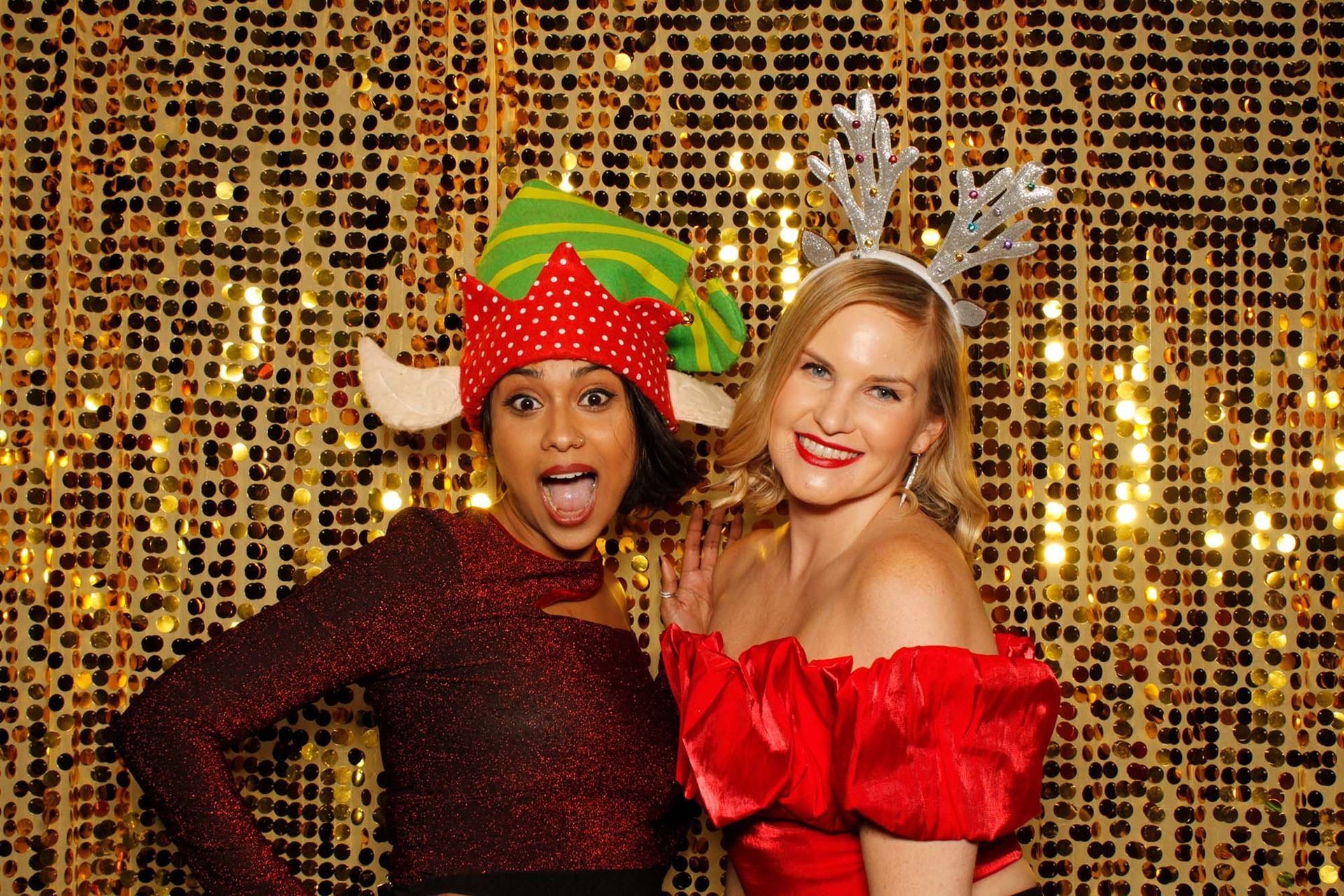 Two people in festive attire posing in front of a gold sequin backdrop.