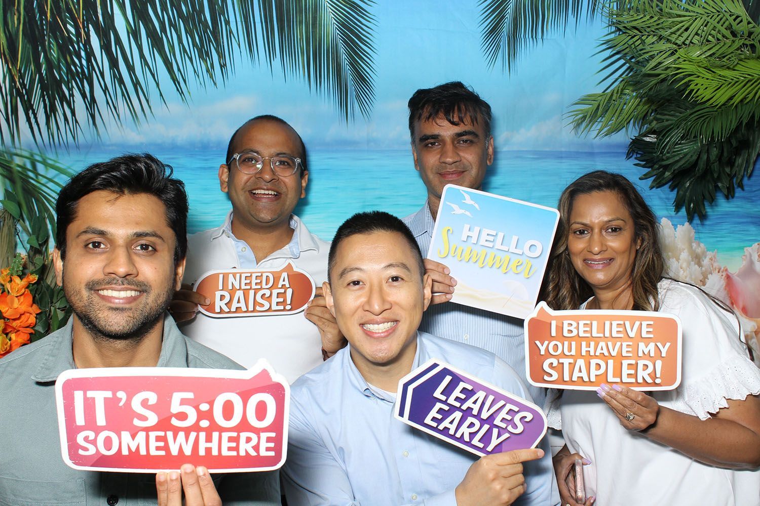Five people in front of a tropical backdrop hold signs with humorous sayings.