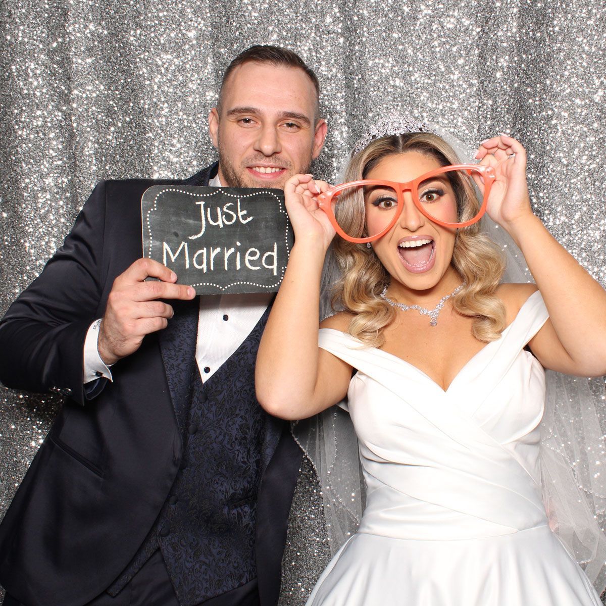 Newlyweds posing in a photo booth with props. Man holds 