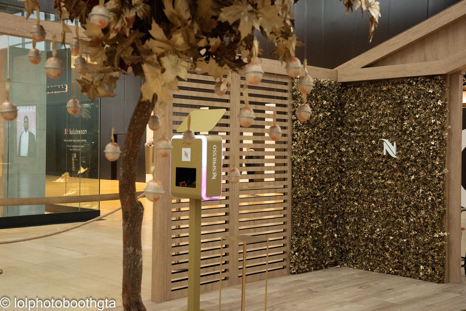 Photo booth in a wooden-themed setup with hanging ornaments and gold foliage.