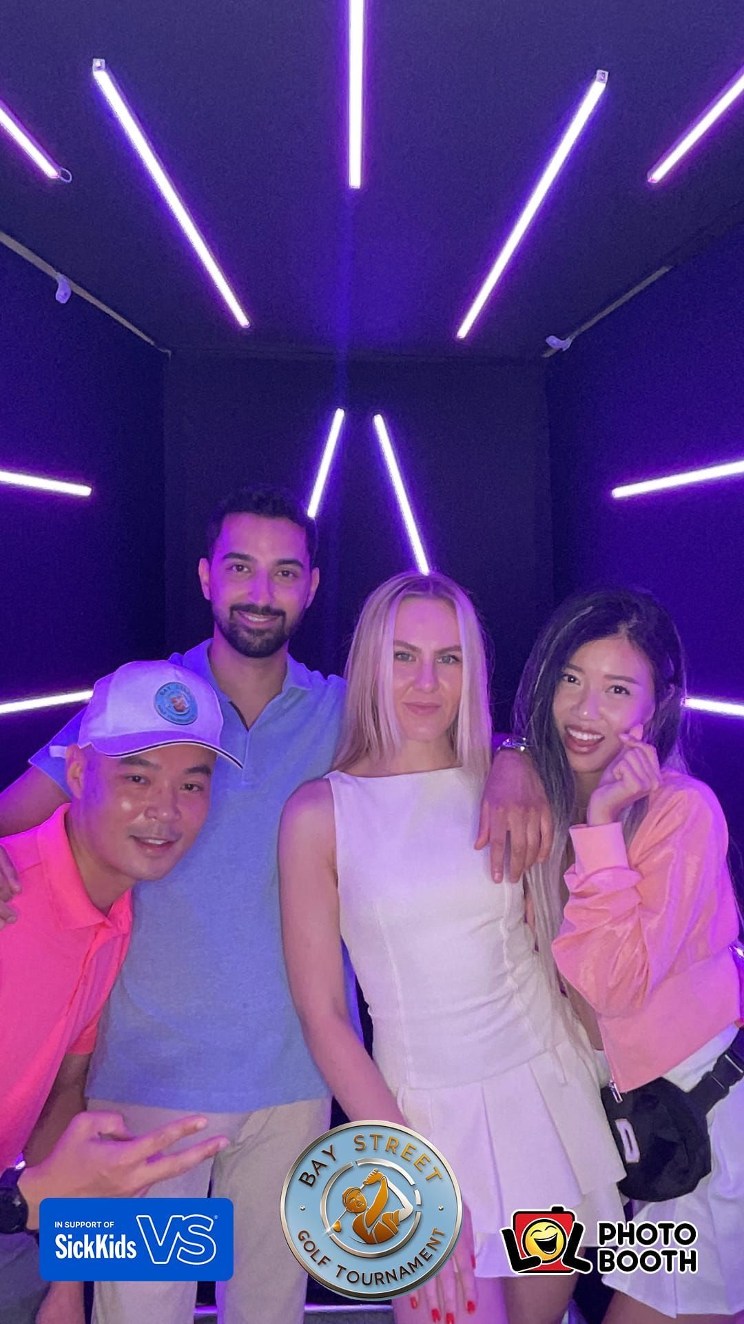 Four people posing in a photo booth with purple neon lights. They are smiling, wearing casual outfits.