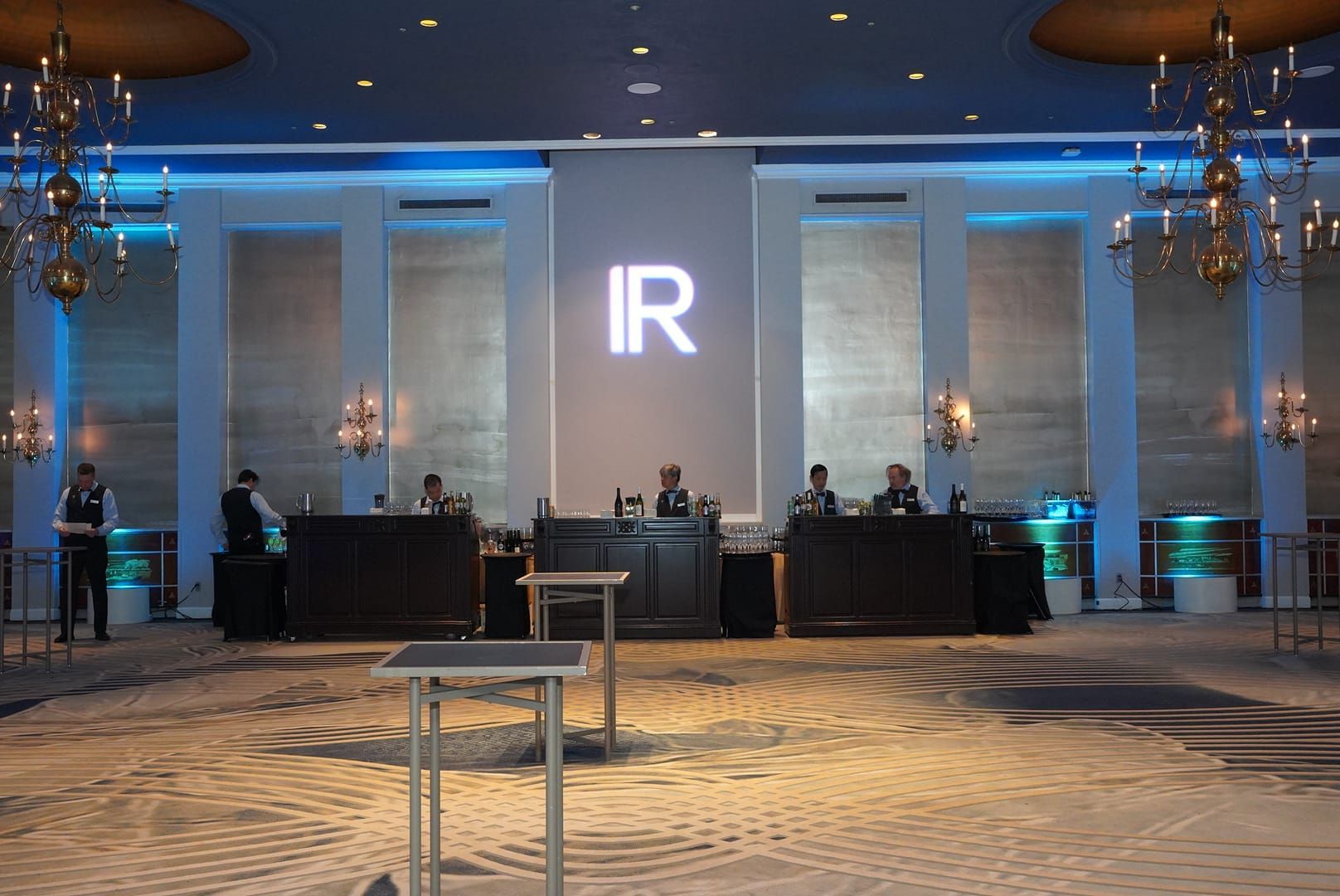 Event setup with large IR logo, staff behind tables, chandeliers, neutral color scheme.