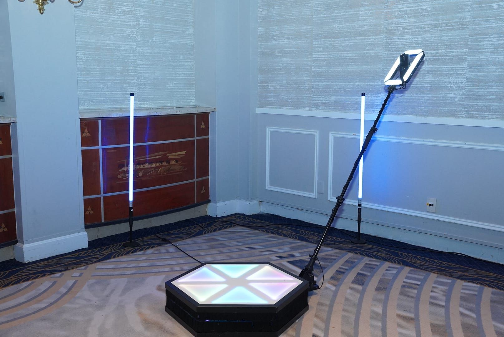A 360 photo booth with a rotating platform and attached phone, surrounded by two light tubes, in a room.