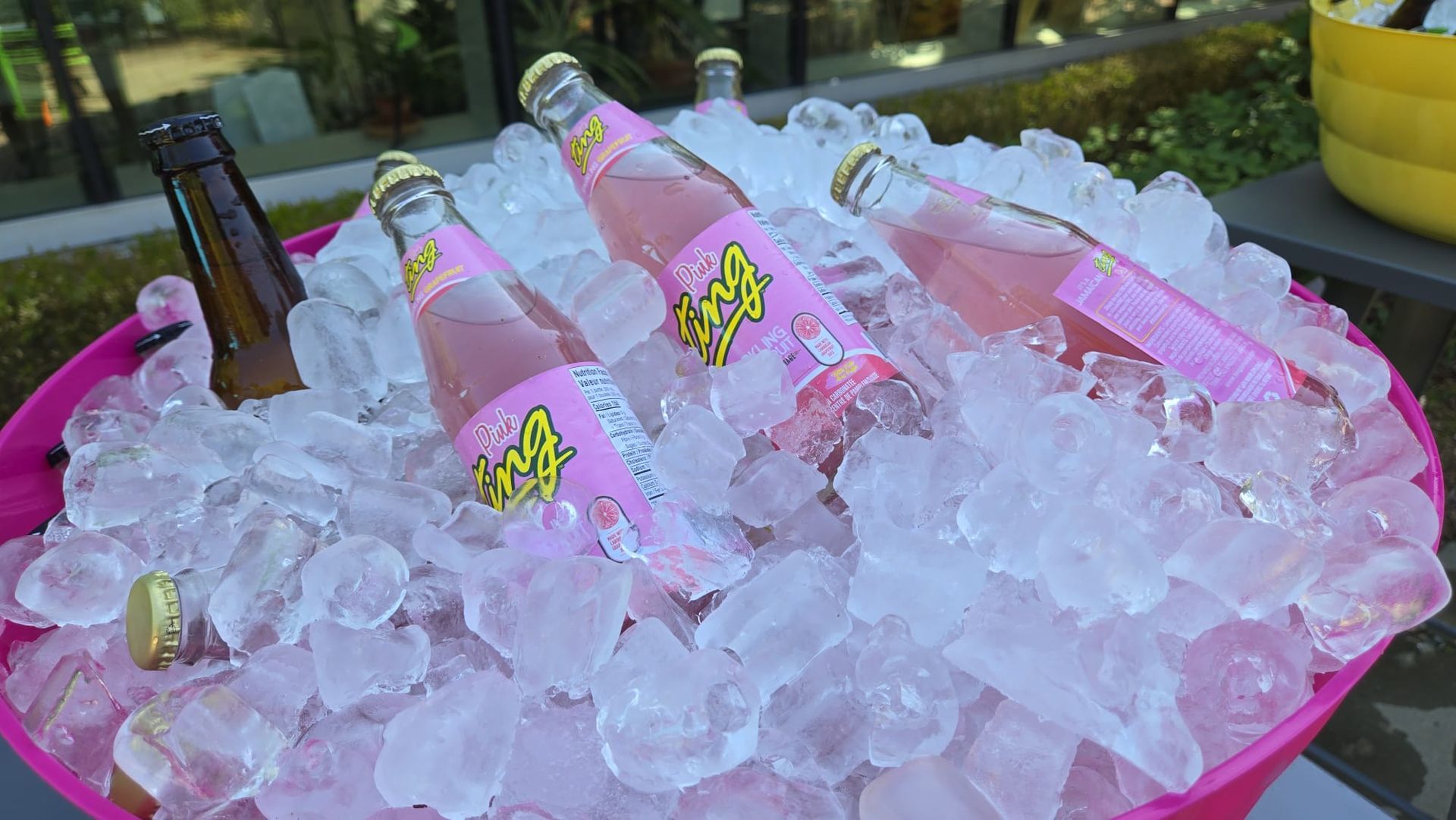 Pink soda bottles in a pink bucket filled with ice, outdoors.