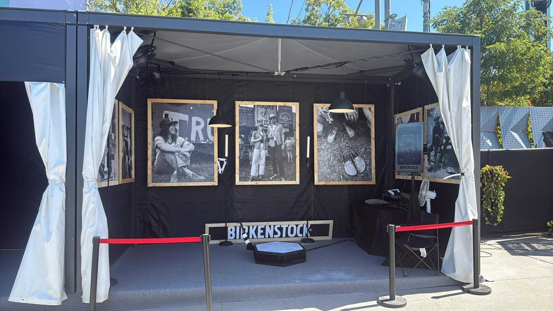 An art display featuring framed black and white photos on a black wall; a red rope barrier.