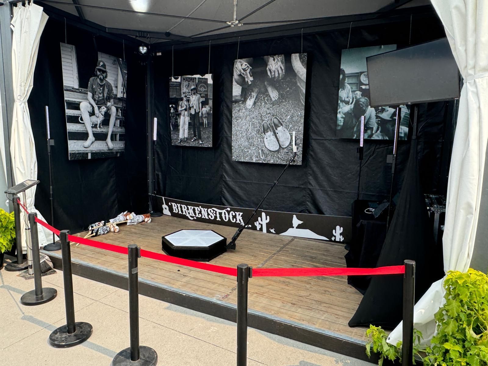 An art exhibit booth with black and white photos, a red rope barrier, and a rotating platform.